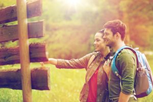 smiling couple at signpost with backpacks hiking small